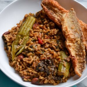 This is a photo of Guyanese cookup rice in a white bowl served with ochro and fried fish and mango achar