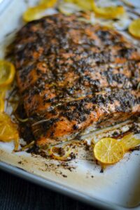 This is a picture of salmon topped with jerk seasonings, lemmon on a white plate