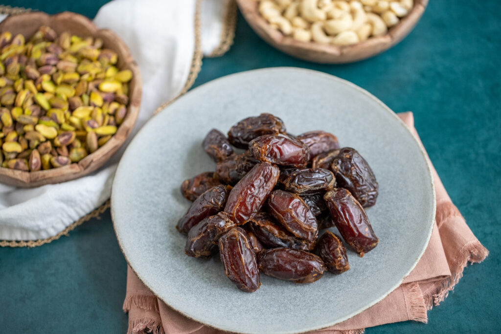 This is a photo of medjool dates in a plate next to pistachios and cashews