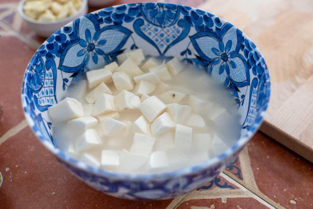 peeled and chopped cassava in a blue bowl covered with water