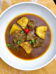 Guyanese beef curry in a white plate on a yellow garnish with wiri-wiri pepper.