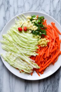 This is an image of cabbage, carrots, garlic, pepper and minced scallions on a white plate for lamb chowmein.