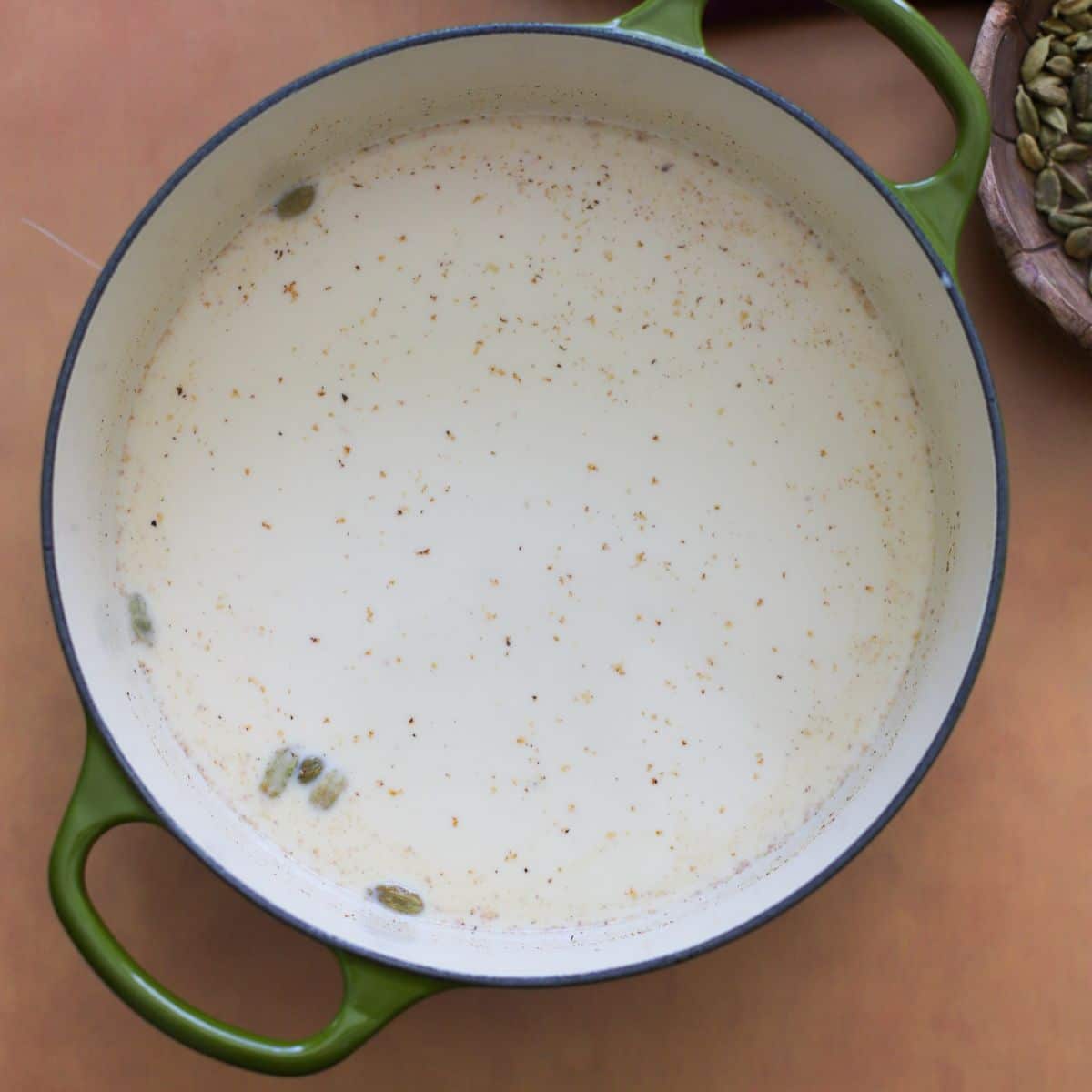 Milk mixture for rasmalai in green pot against a tan background