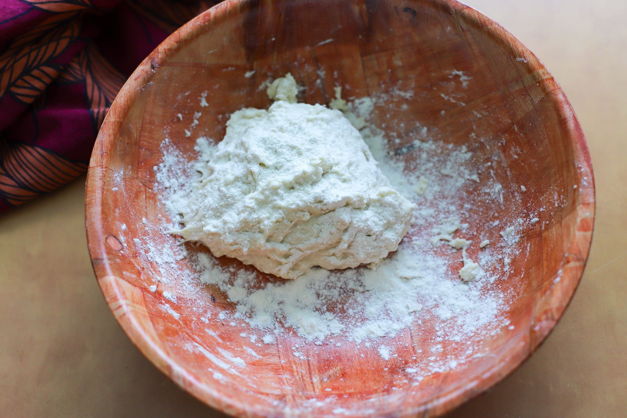a wooden bowl showing a small dough ball with sprinkled flour on top