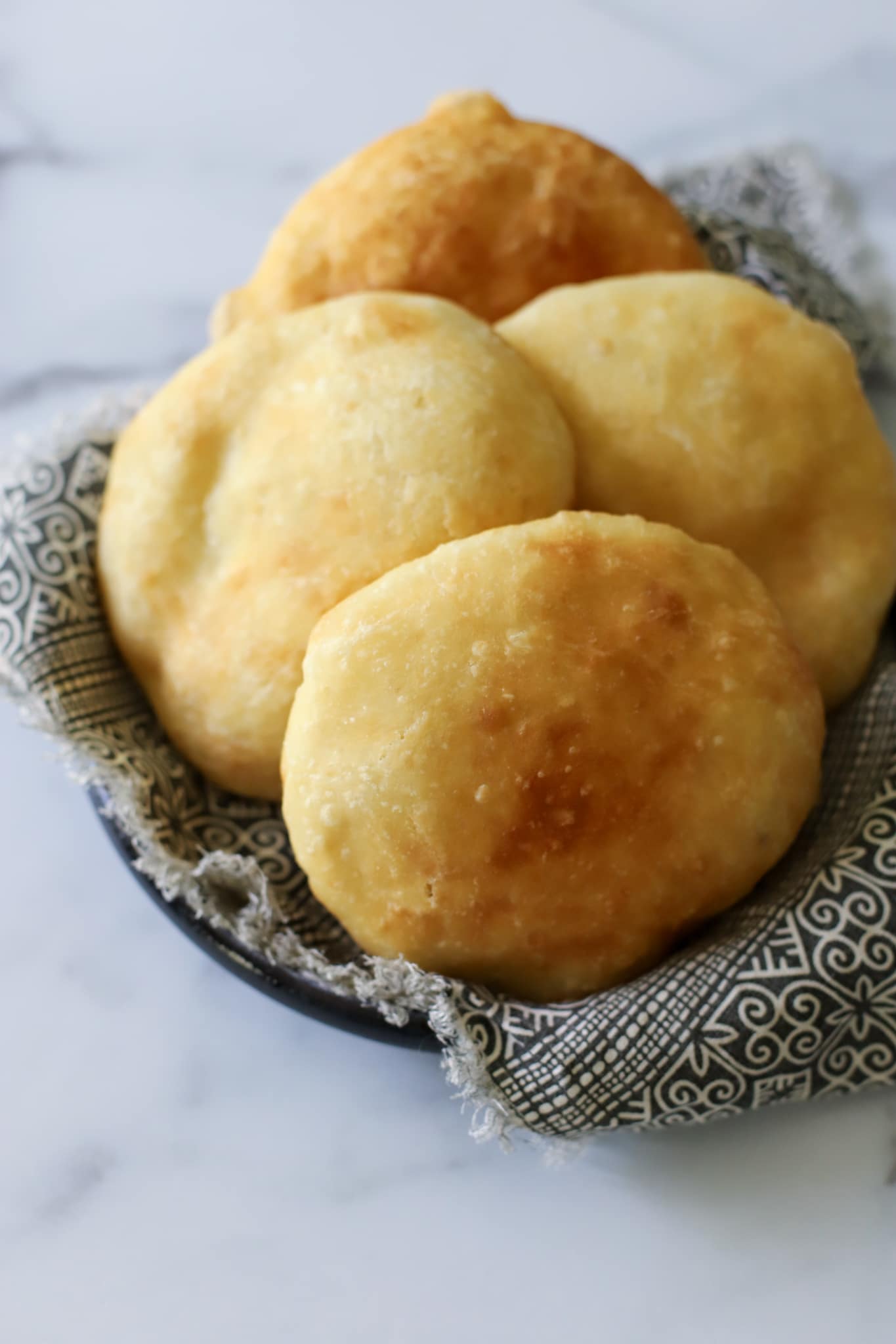 This photo shows a bowl with a napkin holding 4 fried bakes that are golden brown.