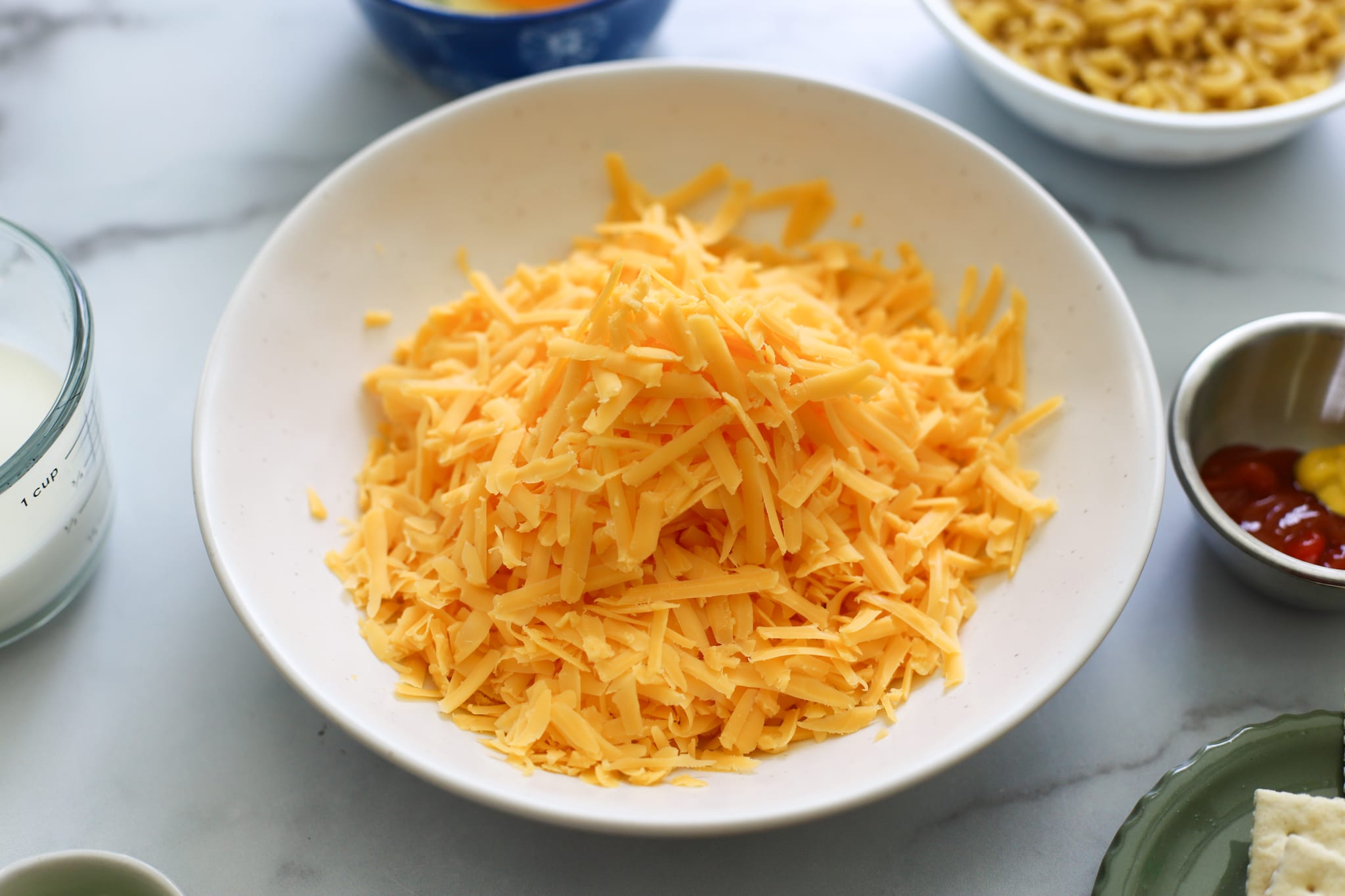 a white bowl of shredded sharp cheddar cheese