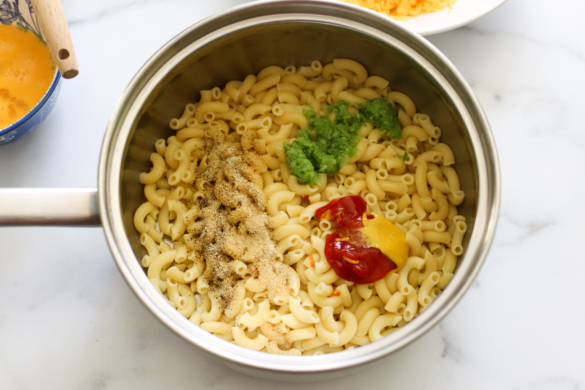 elbow noodles with ketchup mustard black pepper green seasoning in a pot