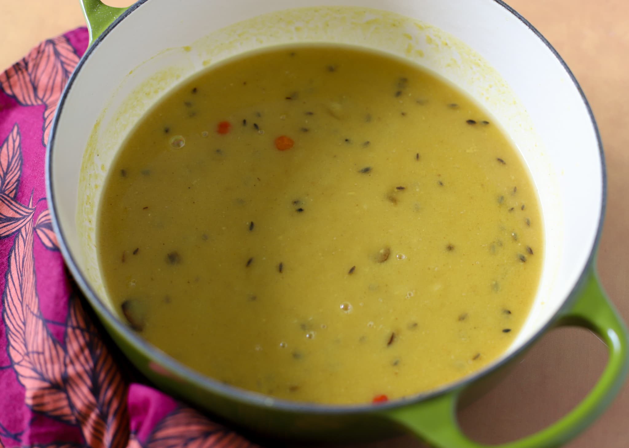 This is a pot of stovetop indo-caribbean style dhal it is in a green cast iron pot with a pink napkin next to it