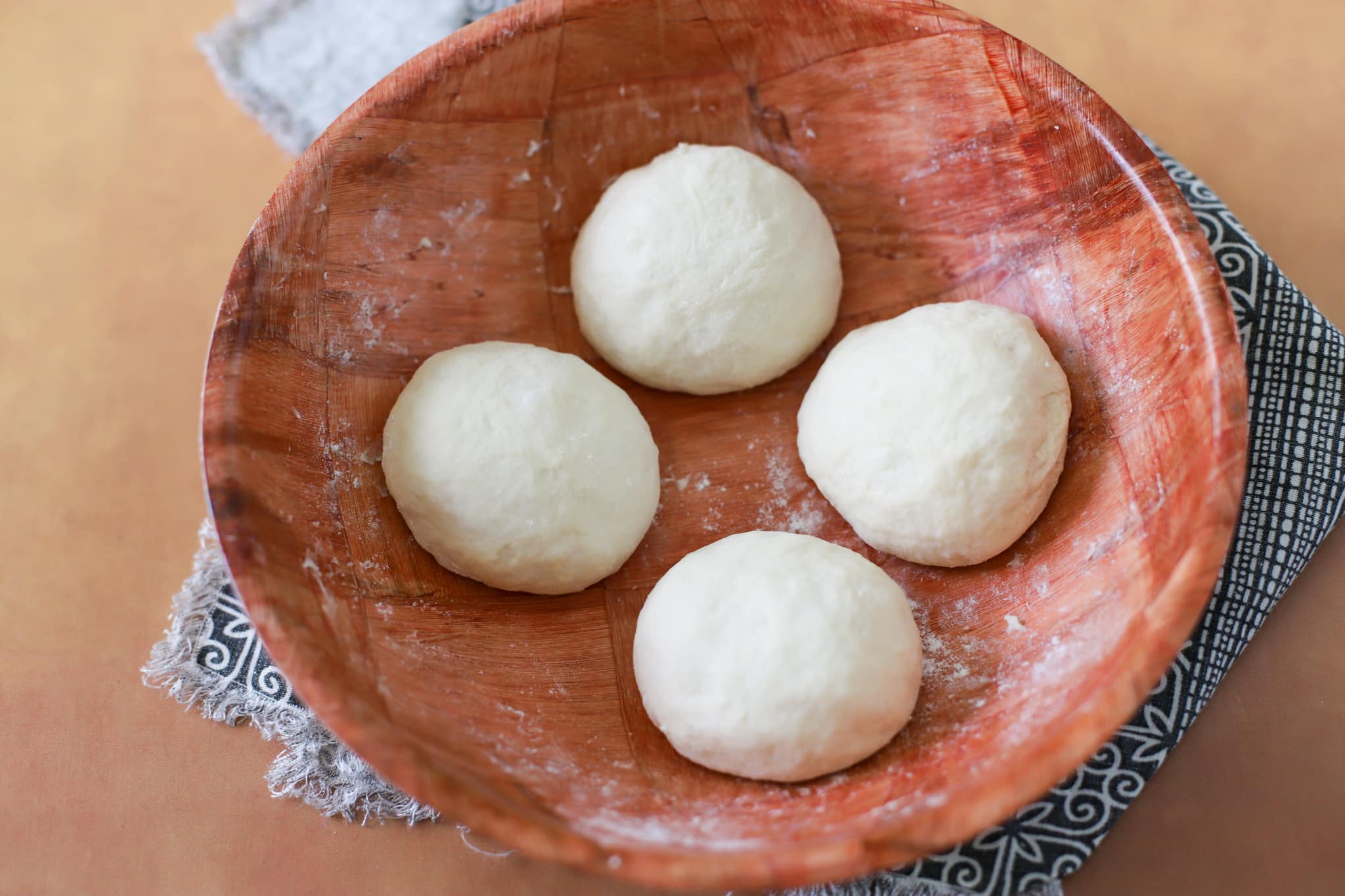 This photo shows a brown bamboo bowl with 4 round dough balls of bake