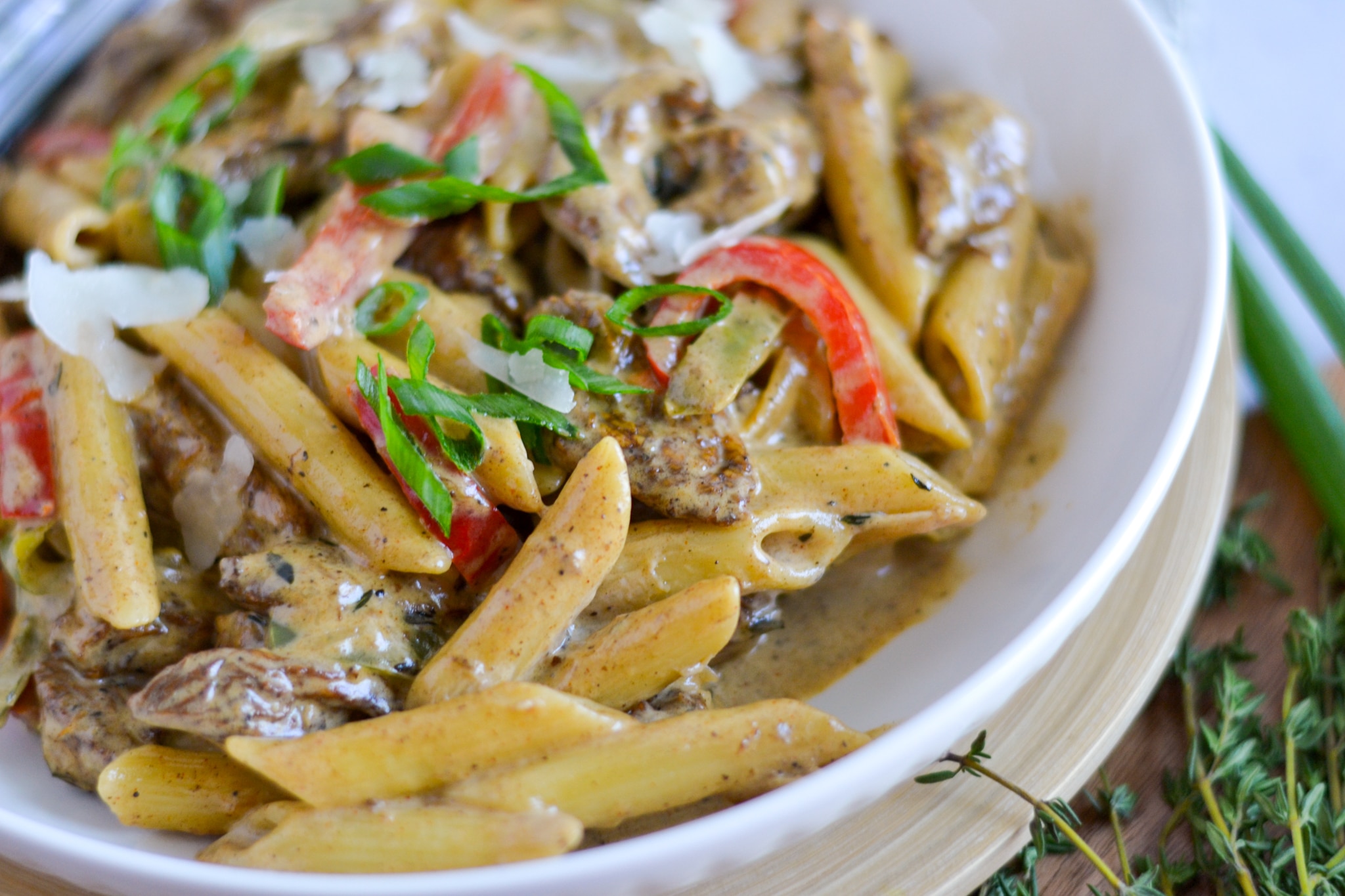 Rasta pasta in a bowl featuring the creamy sauce on the side, penne pasta is smothered in this sauce and topped with chicken, red and green peppers parmesan cheese and scallions