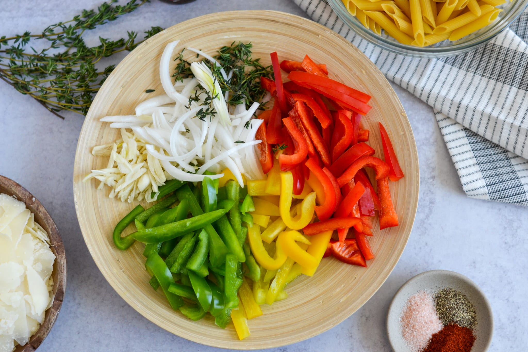 sliced red green yelow bell peppers on a platter with sliced onions, garlic, and thyme leaves