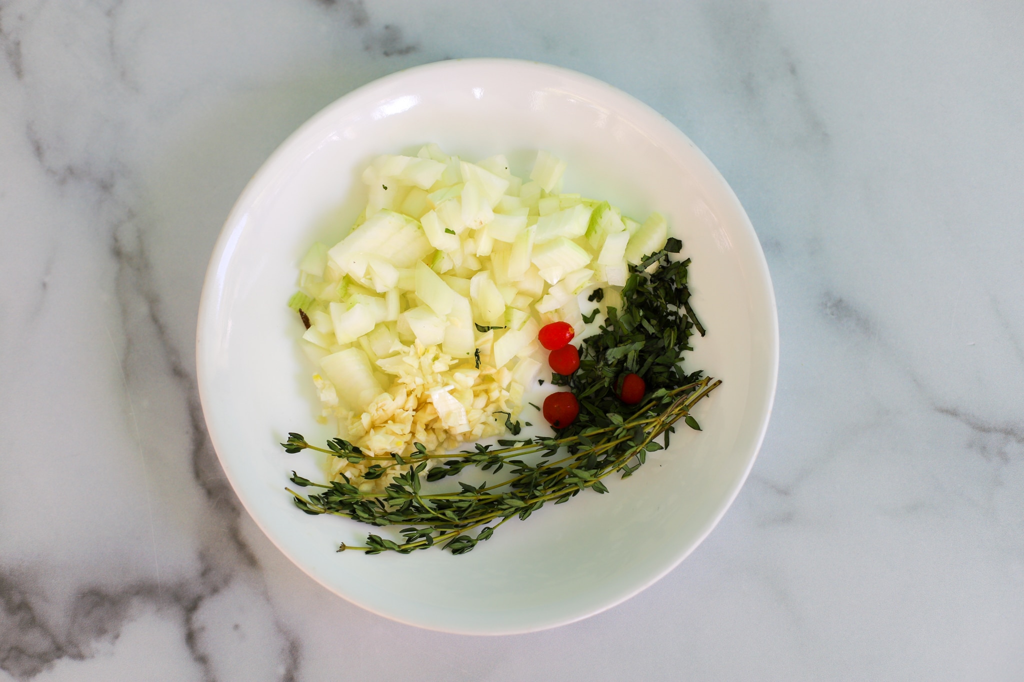 Small batch soup - aromatics in a bowl, the bowl contains diced onions, minced garlic, wiri wiri pepper, parsely, and thyme