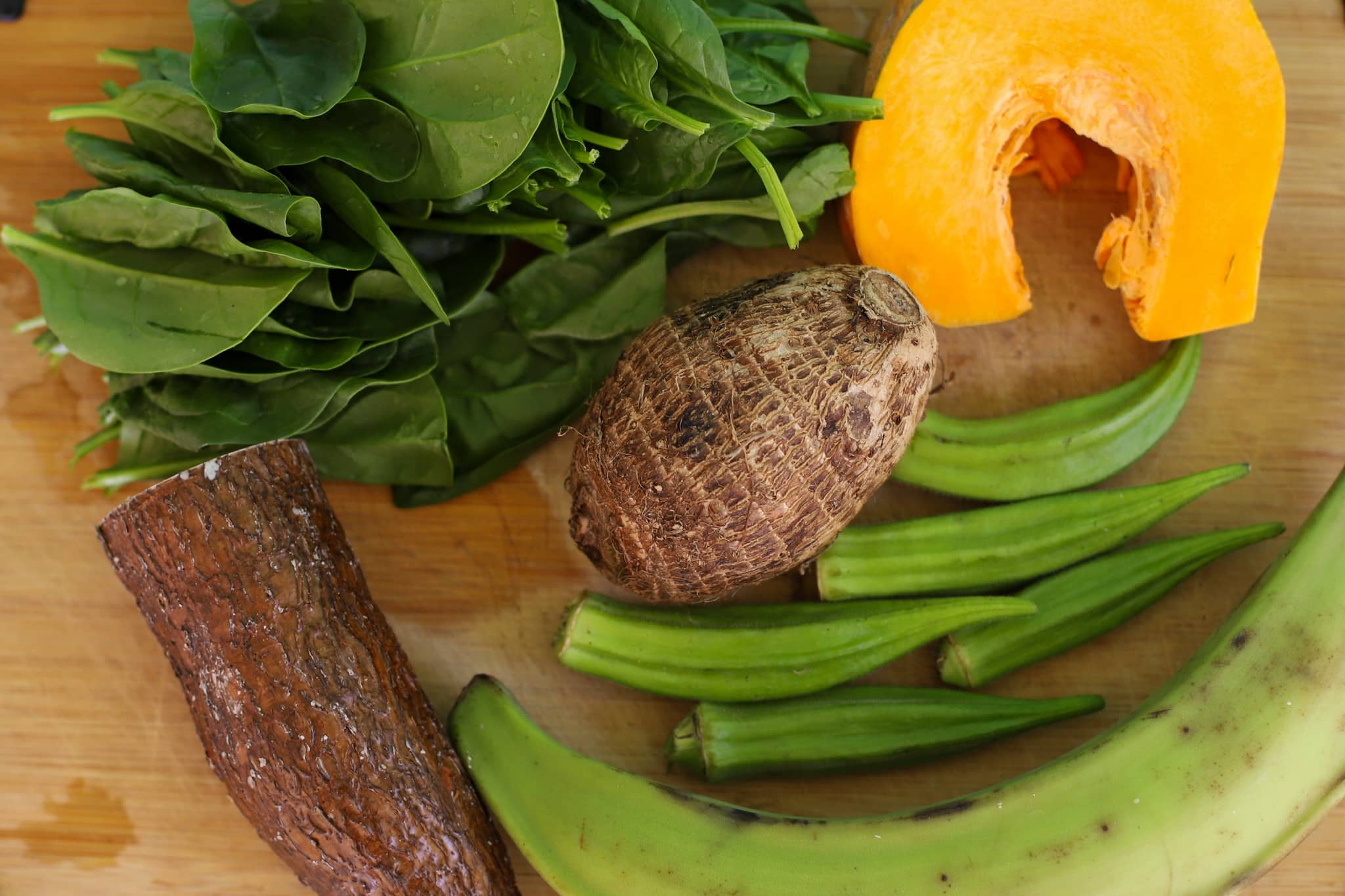 Caribbean vegetables on a cutting board including pumpkin, plantain, okra, edge, spinach, cassava
