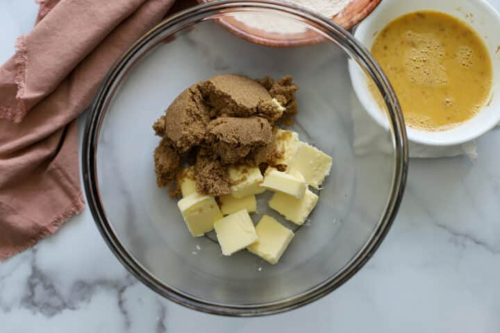 Brown sugar and butter in a mixing bowl next to a white bowl with eggs for making sponge cake
