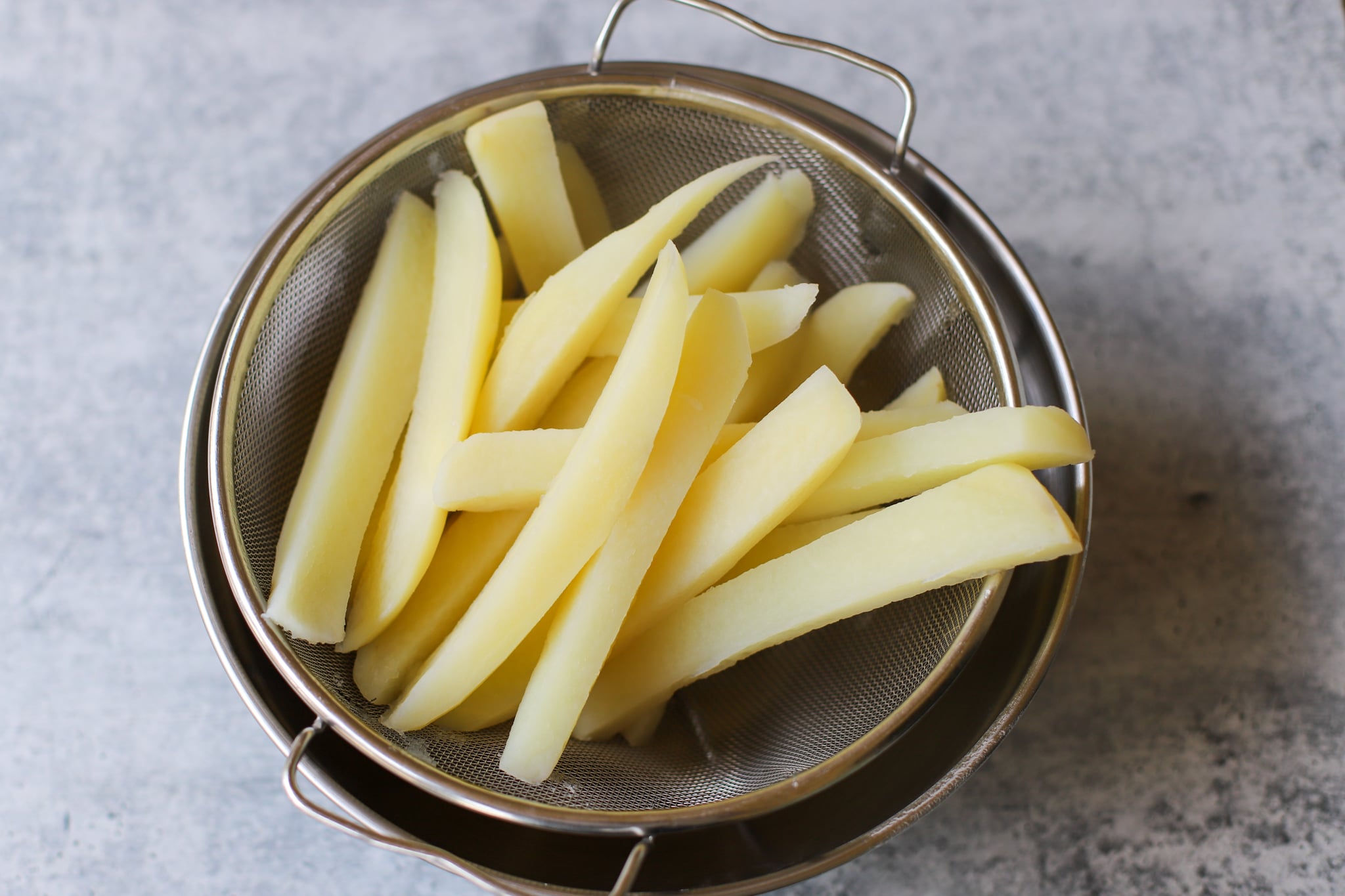 British chips sliced into wedges and being drained after boiling