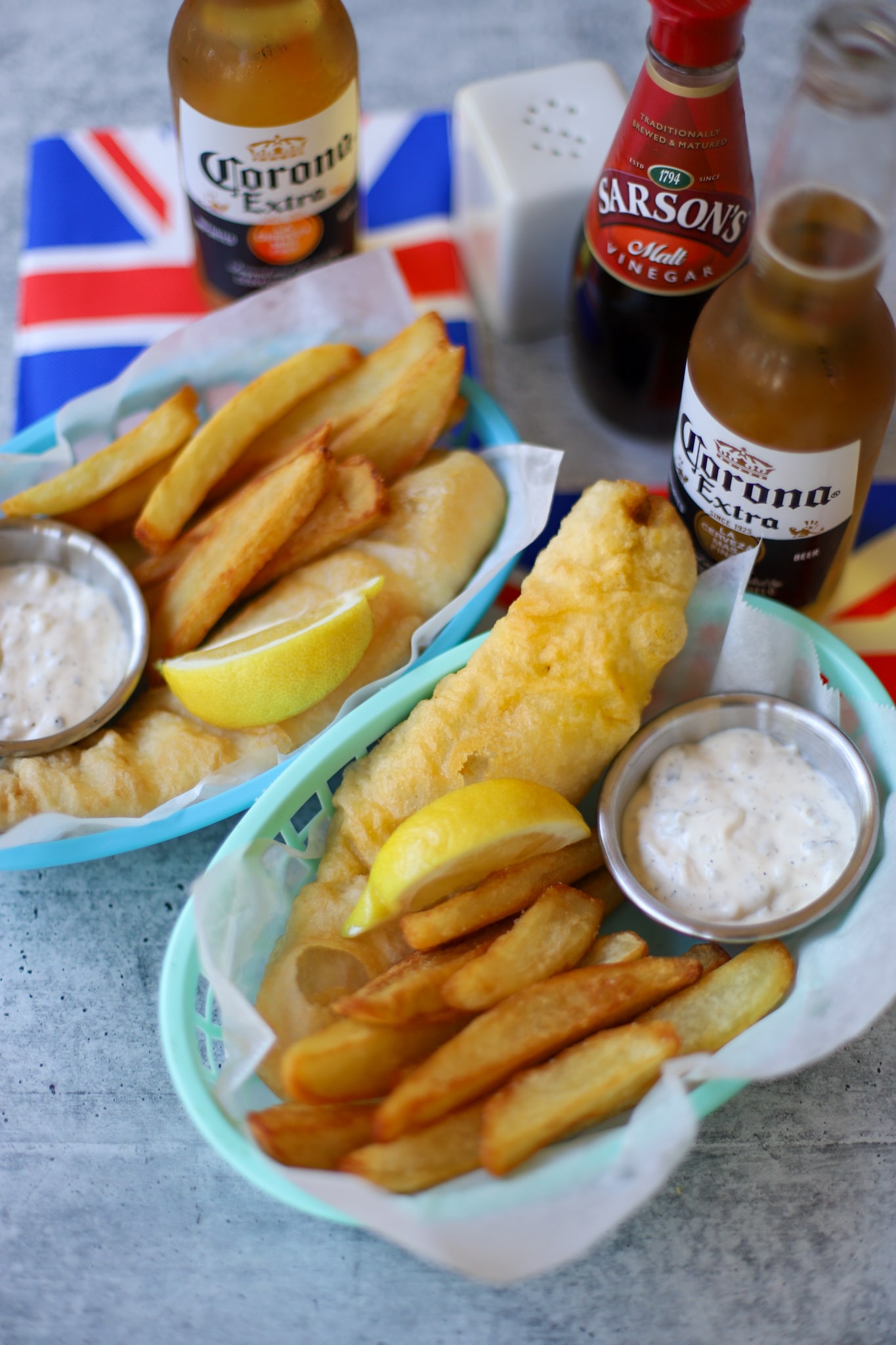 Overhead shot of British fish and chips on a table served with a lemon, tartar sauce malt vinegar and beer