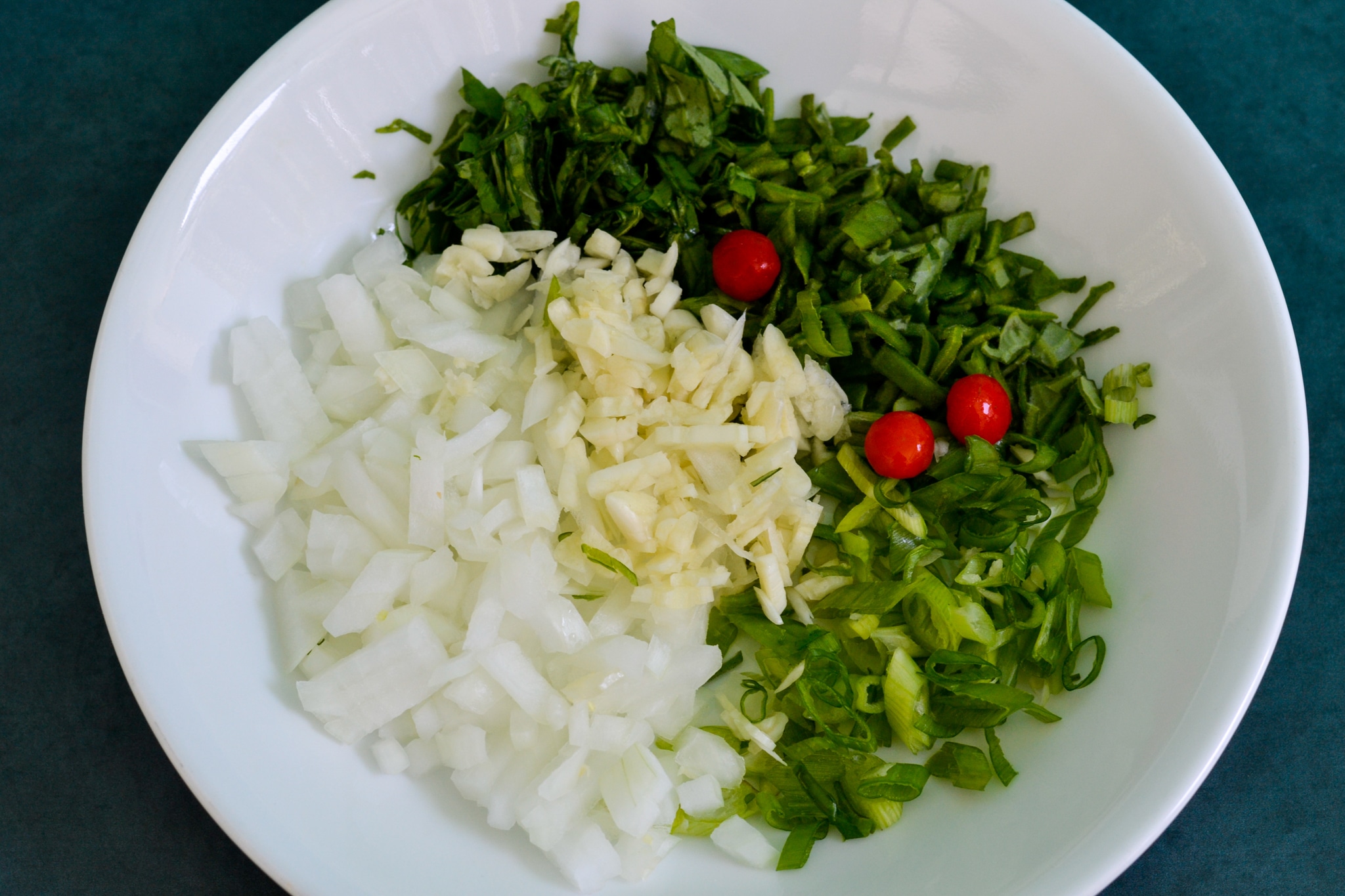Seasoning for cookup rice in a plate. chopped onion, garlic, wiri wiri peppers, broad leaf thyme, scallions, and basil.
