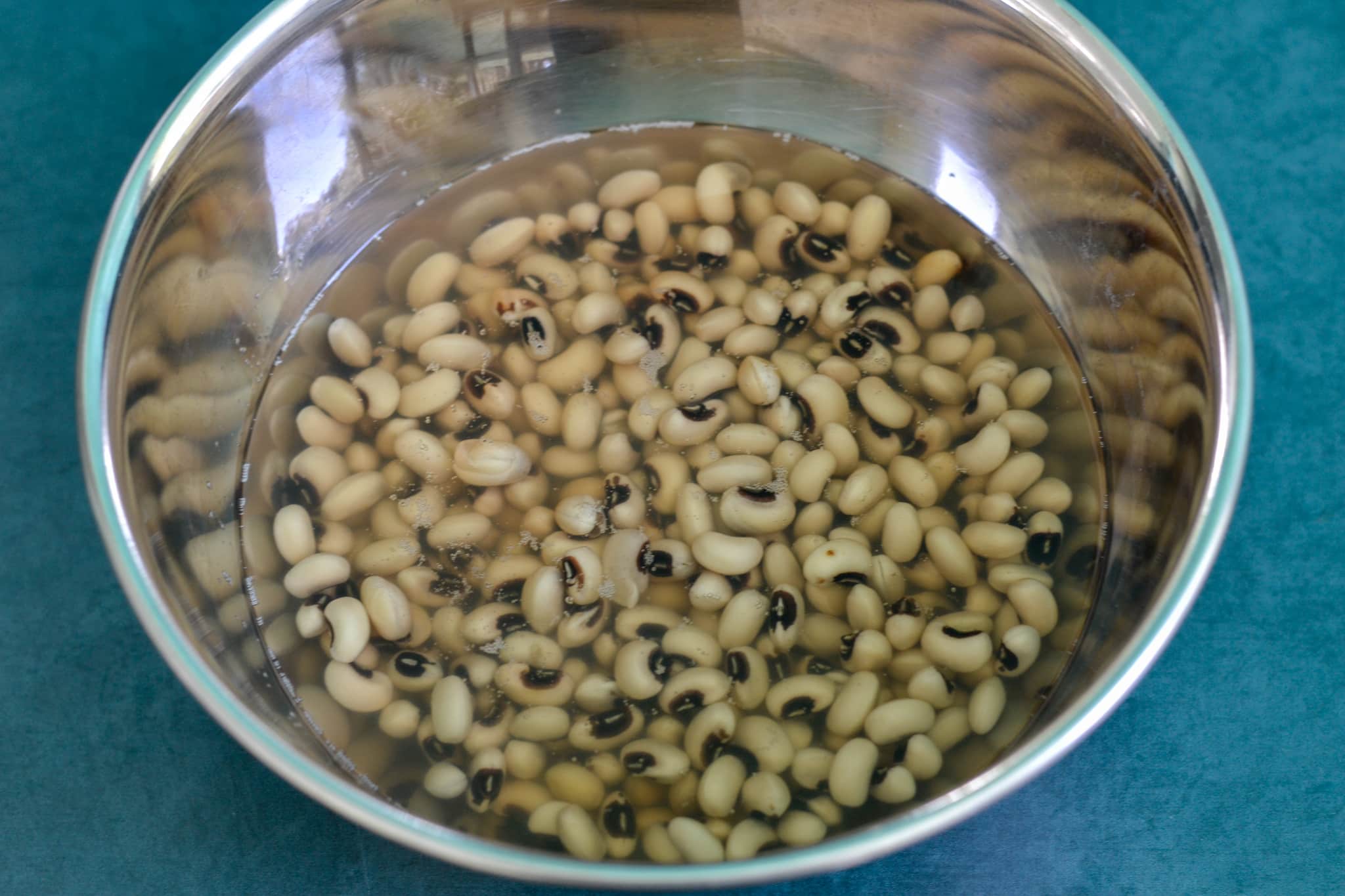 A silver mixing bowl with dried black eyed peas soaking in water