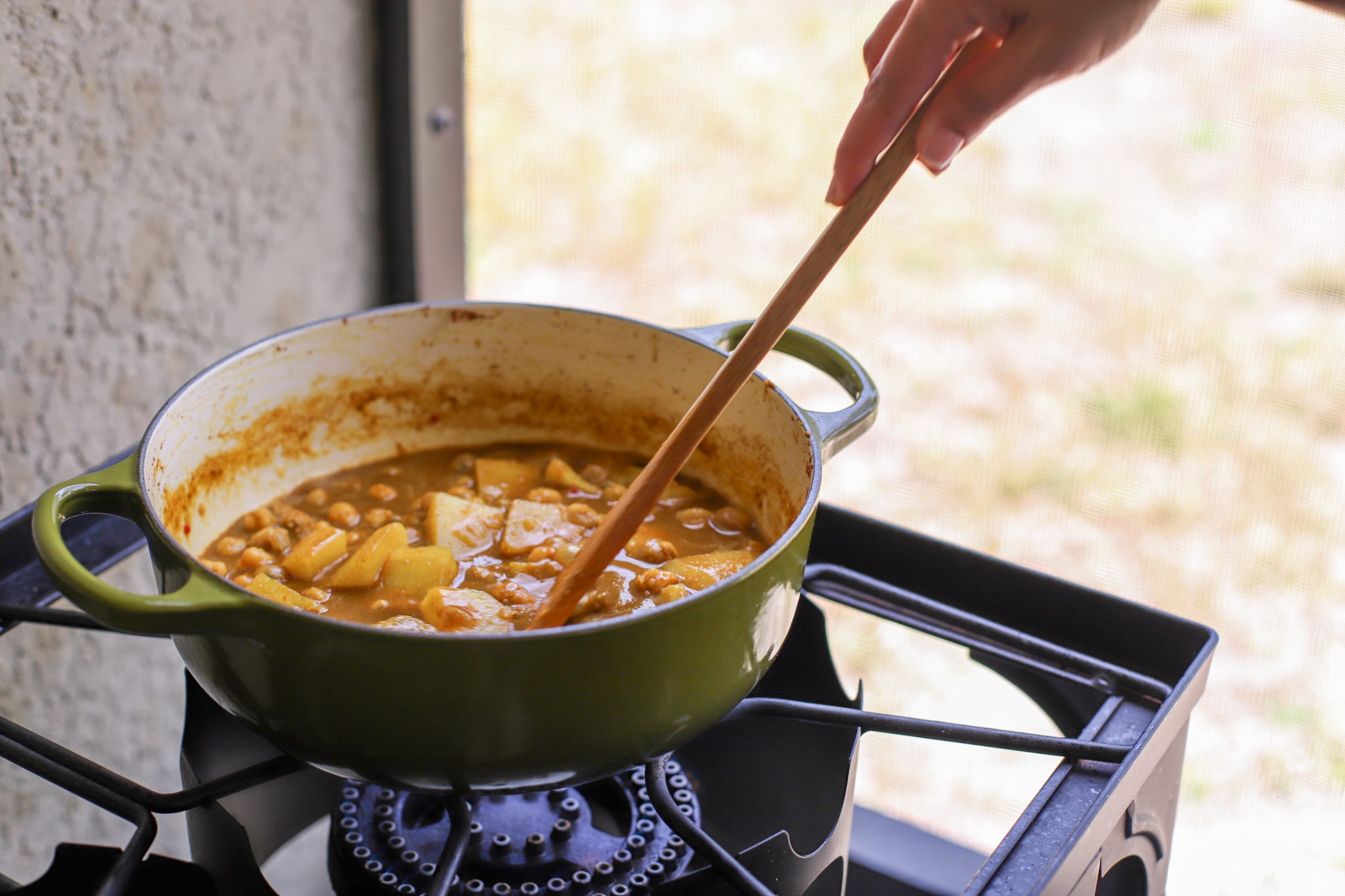channa curry simmering on the stovetop in green pot being turned by a wooden spoon