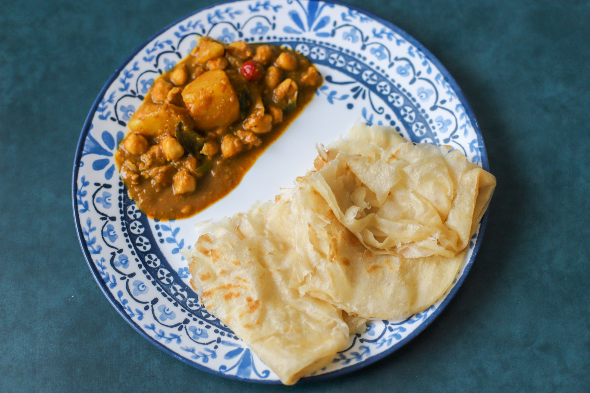 channa curry served with flaky oil roti in a blue chinoiserie plate