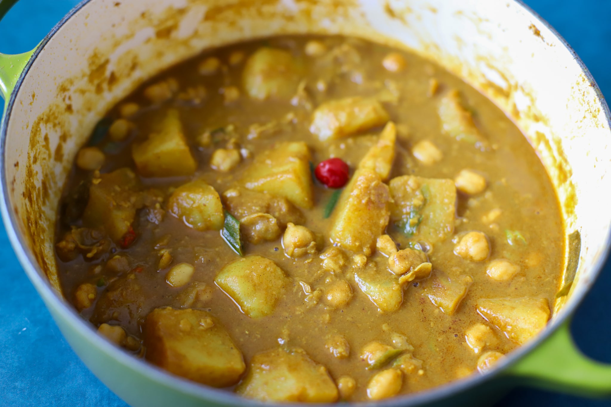 Channa curry in a green pot garnished with wiri wiri pepper